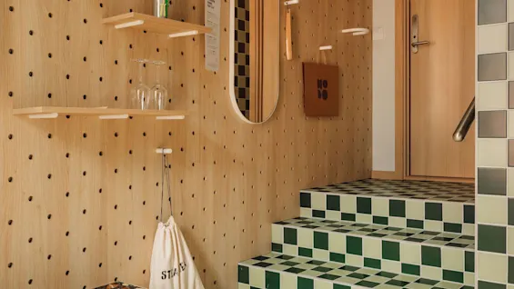 A vibrant entryway at hobo oslo with a wooden pegboard wall, green and light green checkered stairs, and a bench. 