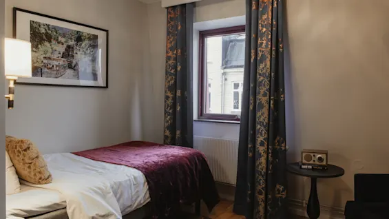 A comfortable hotel room at Home Hotel Kung Oscar featuring a single bed, patterned curtains, and a radio on a side table.
