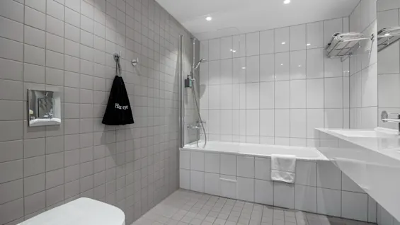 Moderne bad i Deluxe-rom på Comfort Hotel Porsgrunn med toalett, badekar og vask. En pose med 'Har ry' henger på veggen.