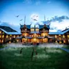 Spøgelsesagtigt hotel om natten med fuldmåne, flagermus og zombiehænder, der stikker op af tåget græs.