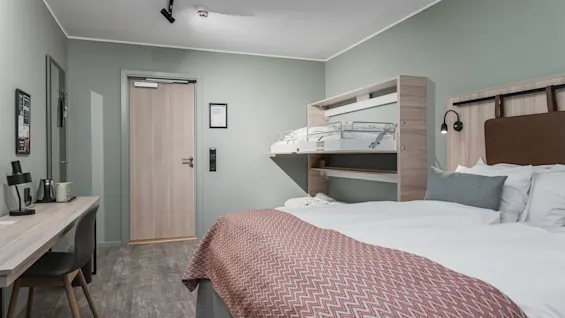 Et moderne hotellrom med en komfortabel seng, et skrivebord og en smart køyeseng for ekstra gjester.
