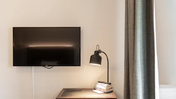 Kotoisa työpöytäalue Home Hotel Victoriassa, jossa on televisio, lamppu ja kirjoja, työhön tai rentoutumiseen.