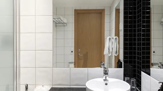 A clean and modern bathroom featuring a white sink, a large mirror, and contrasting white and black tiled walls.