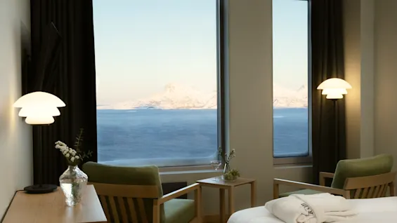 Hyggeligt hotelværelse med fantastisk udsigt over sneklædt bjerg og roligt hav, komfortable siddepladser og seng med badekåbe.