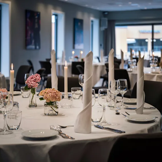 En elegant spisesal med runde bord dekket for et formelt arrangement, med hvite duker, levende lys og blomsteroppsatser.