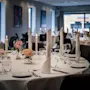 An elegant dining room with round tables set for a formal event, featuring white tablecloths, candles, and floral centerpieces.