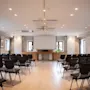 Konferanserom med rader av tomme stoler vendt mot en stor projektorskjerm. Rommet er godt opplyst med taklys og har innrammede bilder og vinduer i en moderne setting.