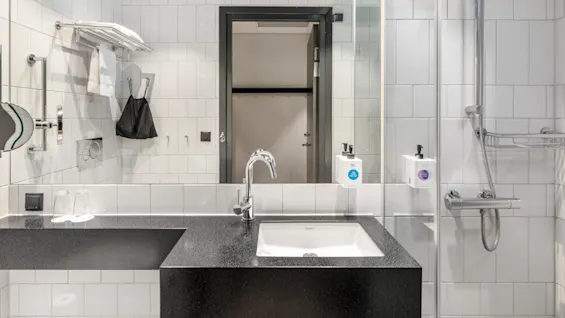 Et rent og moderne hotelbadeværelse med vask, spejl og bruser, designet til gæsternes komfort.
