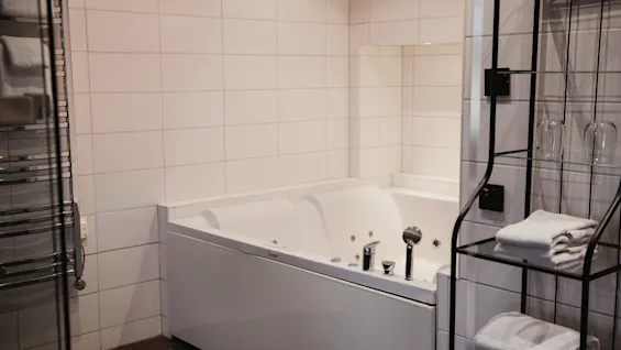 Puhdas, moderni kylpyhuone, jossa on suuri valkoinen poreamme, pyyhekuivain ja hylly, jossa on puhtaita pyyhkeitä ja laseja.