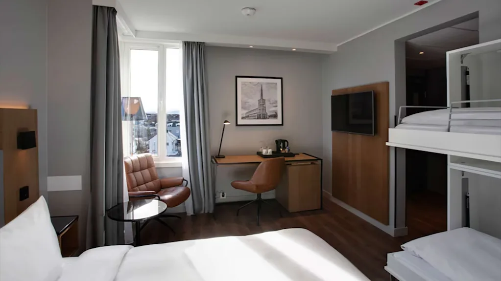 Lyst og moderne familierom med en dobbeltseng, køyesenger, et skrivebord og en behagelig lenestol ved vinduet.