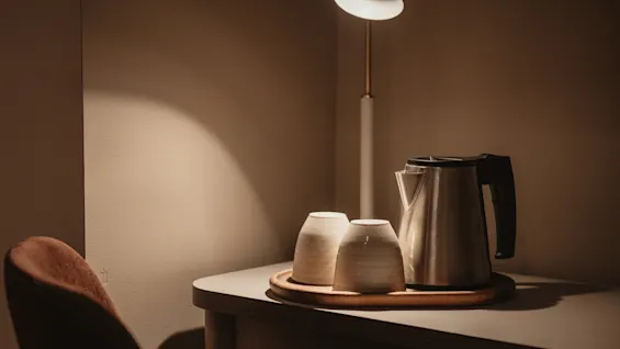 En mysig hörna med en vattenkokare och två koppar på en träbricka, upplyst av en varm lampa, redo för en avkopplande dryck.