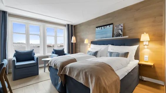 Et hotellrom med to senger, lenestoler og et stort vindu som tilbyr en naturskjønn utsikt over vannet.