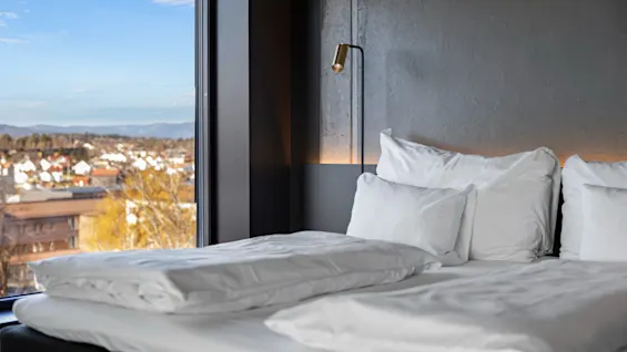 En koselig seng med hvitt sengetøy på Comfort Hotel Porsgrunn, med utsikt over byen og fjellene.