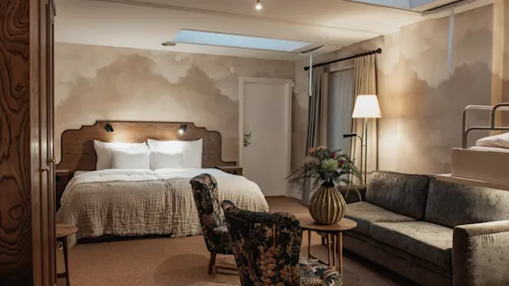 Home Hotel Baltzar - Family Room. A cozy hotel room with a large bed, sofa, armchairs, and an elevated sleeping area.