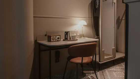 En mysig skrivbordshörna på hotellrummet med lampa, radio och kaffe/te-utrustning, bredvid en öppen garderob med strykbräda.