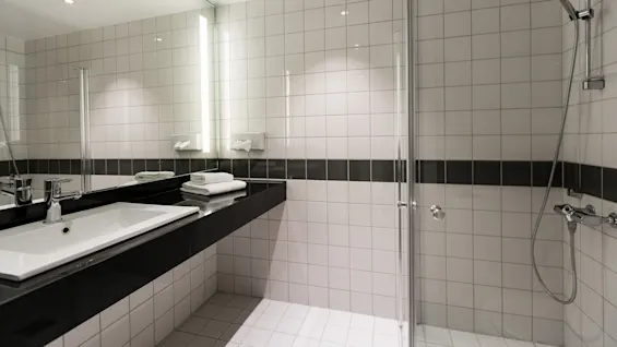Sink with a chrome faucet, surrounded by a spacious countertop featuring neatly folded towels, adjacent to a glass-enclosed shower with modern fixtures; all set in a tiled bathroom.