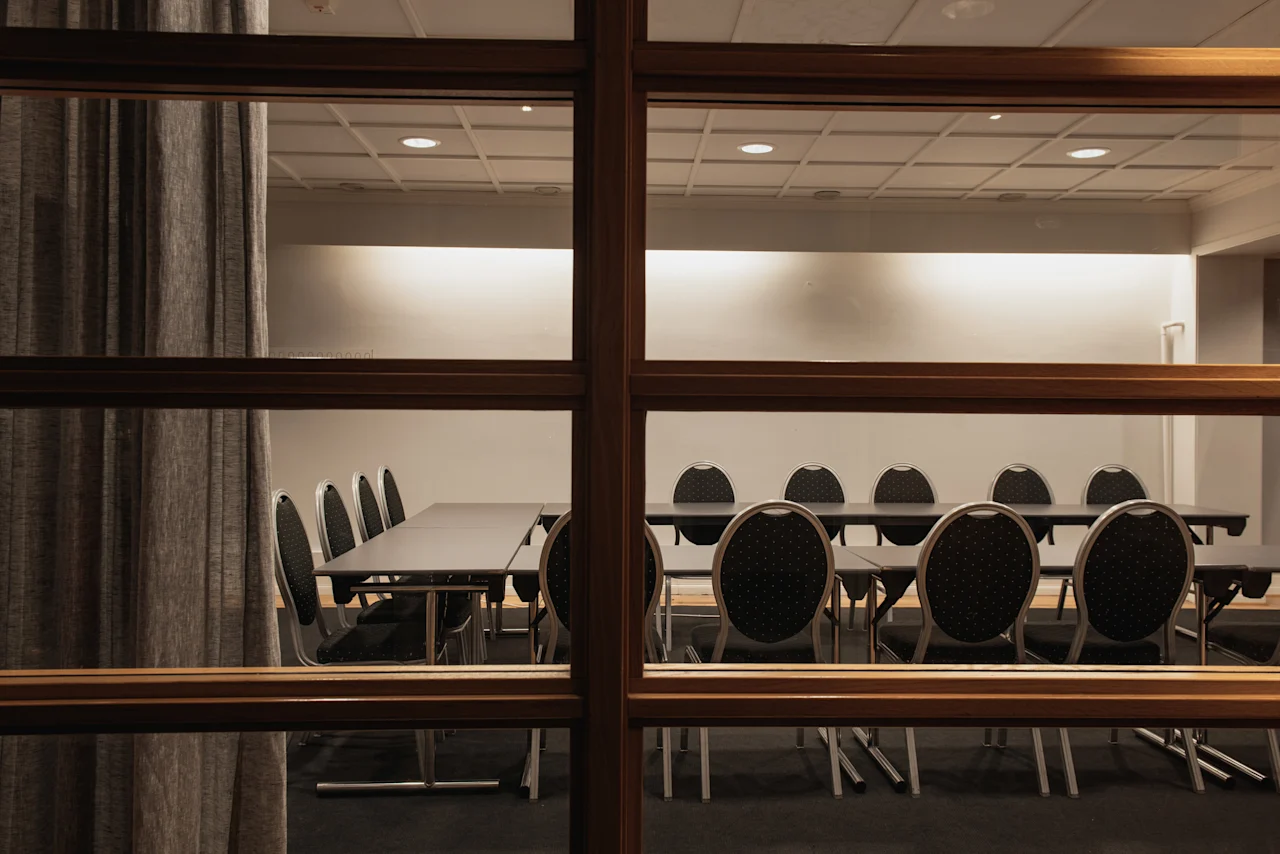 Ett konferensrum med flera bord och stolar, sett genom ett fönster på Home Hotel Grand, Helsingborg.