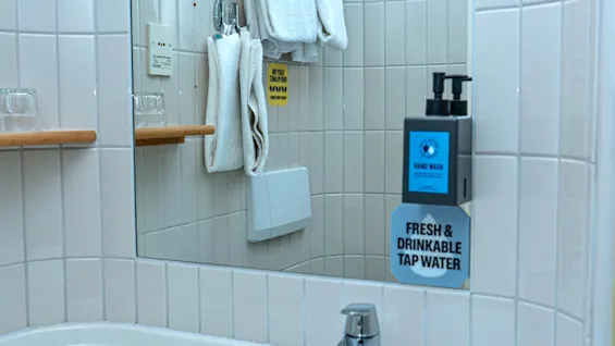Ett badrum med handfat, spegel, handtvål och en skylt som säger HAND WASH FRESH AND DRINKABLE TAP WATER.