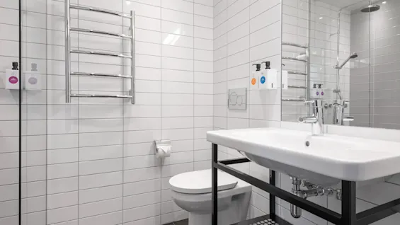 A well-lit, modern bathroom with white tiled walls, a sink, toilet, and a heated towel rack.