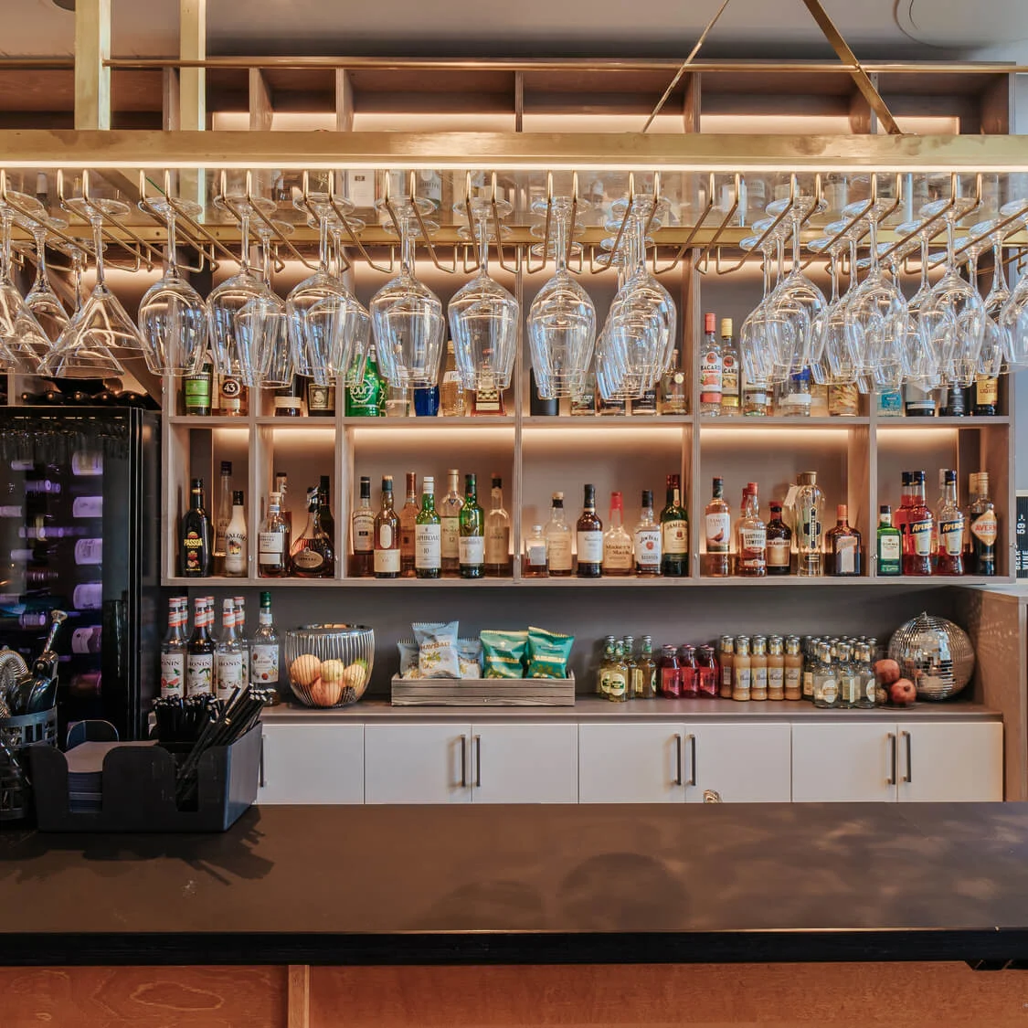 Glasses hang above a bar counter, stocked with bottles, mixers, and snacks. A sign reads, "Welcome to the dark side. Porter proving. Fredagen 29/9. Boka din plats här."