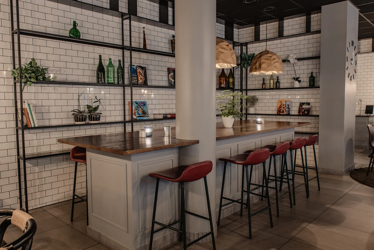 Tyylikäs baarialue, jossa on pitkä tiski, punaiset tuolit ja koriste-esineillä koristellut hyllyt.