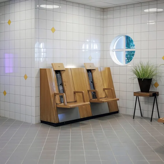 Et moderne, flislagt avslapningsområde i et spa med infrarøde trestoler, potteplanter og runde vinduer.