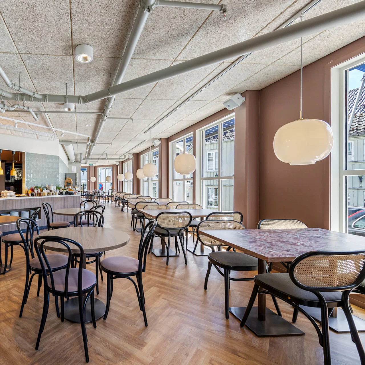 A modern café interior with wooden floors, round hanging lights, and tables with chairs, large windows provide natural light.