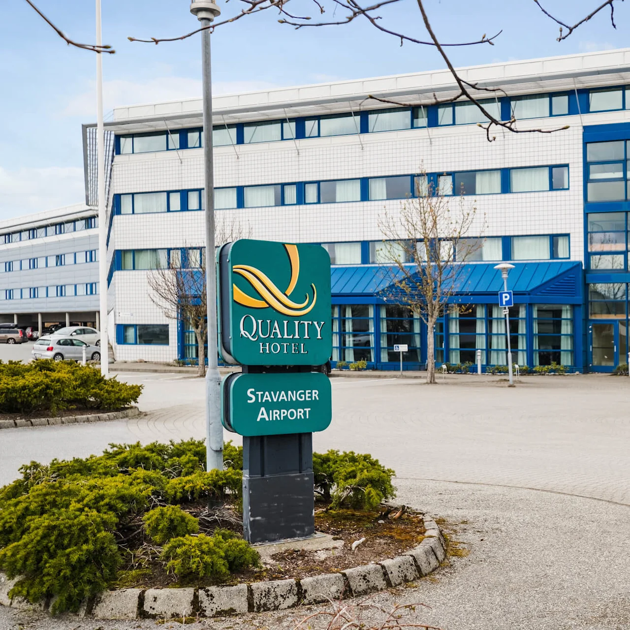 A hotel facade with a prominent sign reading "Quality Hotel" and "Stavanger Airport" in an empty parking lot during the day.