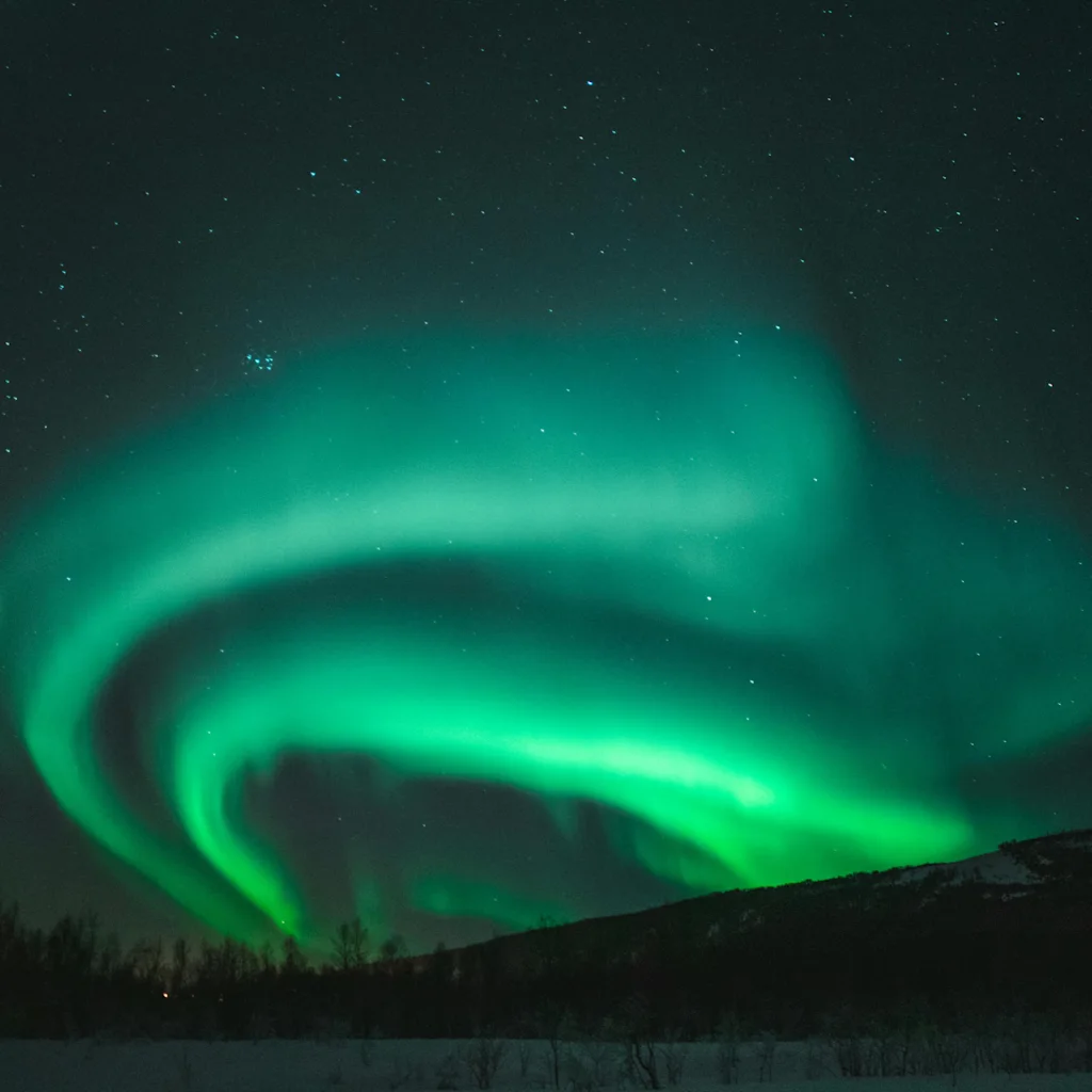 Revontulten lumoava vihreä hehku valaisee pimeää, tähtikirkasta yötaivasta rauhallisen, lumipeitteisen maiseman yllä.