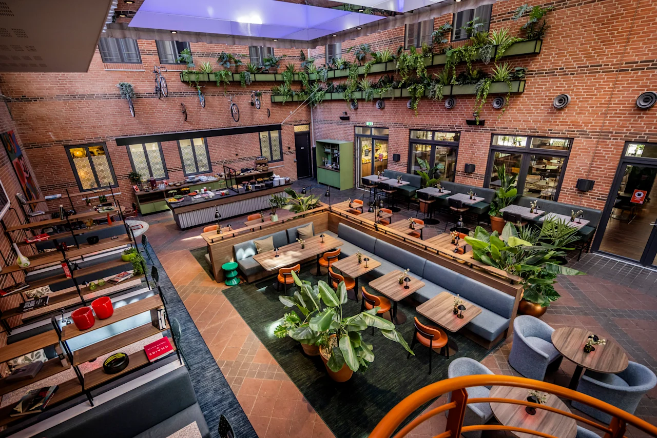 A vibrant hotel lobby and restaurant area at Comfort Hotel Vesterbro, featuring brick walls, lush greenery, and diverse seating.