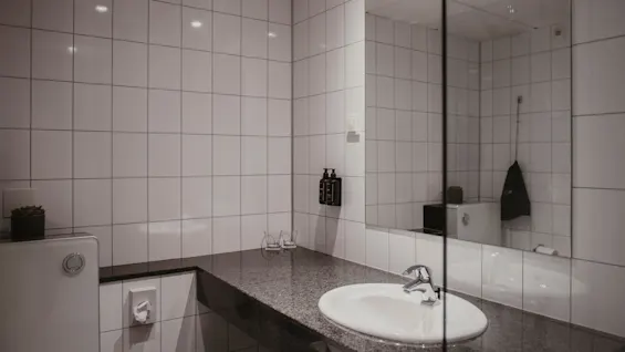 Et rent og moderne hotelbadeværelse med vask, spejl og hvide flisevægge, klar til brug.