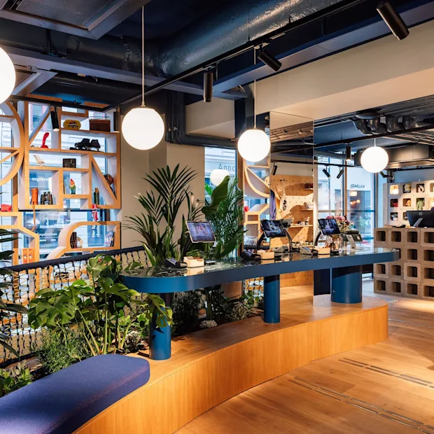 Hobo Oslo, resepsjon. A modern hotel lobby with a person at the reception desk, self-service stations, and lush plants.