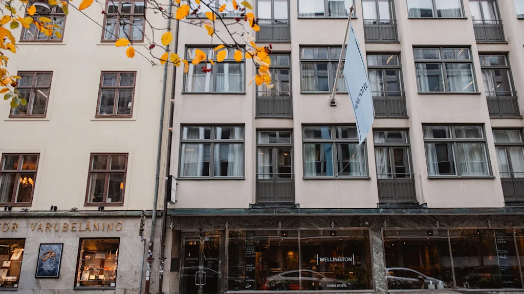 Eksteriør af Home Hotel Wellington i Stockholm med flag og efterårsblade. Stueetagen har store vinduer.