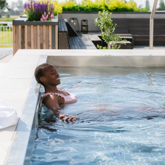 En person kopplar av i en pool med slutna ögon och njuter av vattnet utomhus.