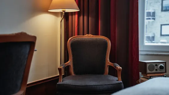 En mysig hörna med en fåtölj, varmt lampljus och en radio på böcker vid ett fönster. Perfekt för avkoppling.