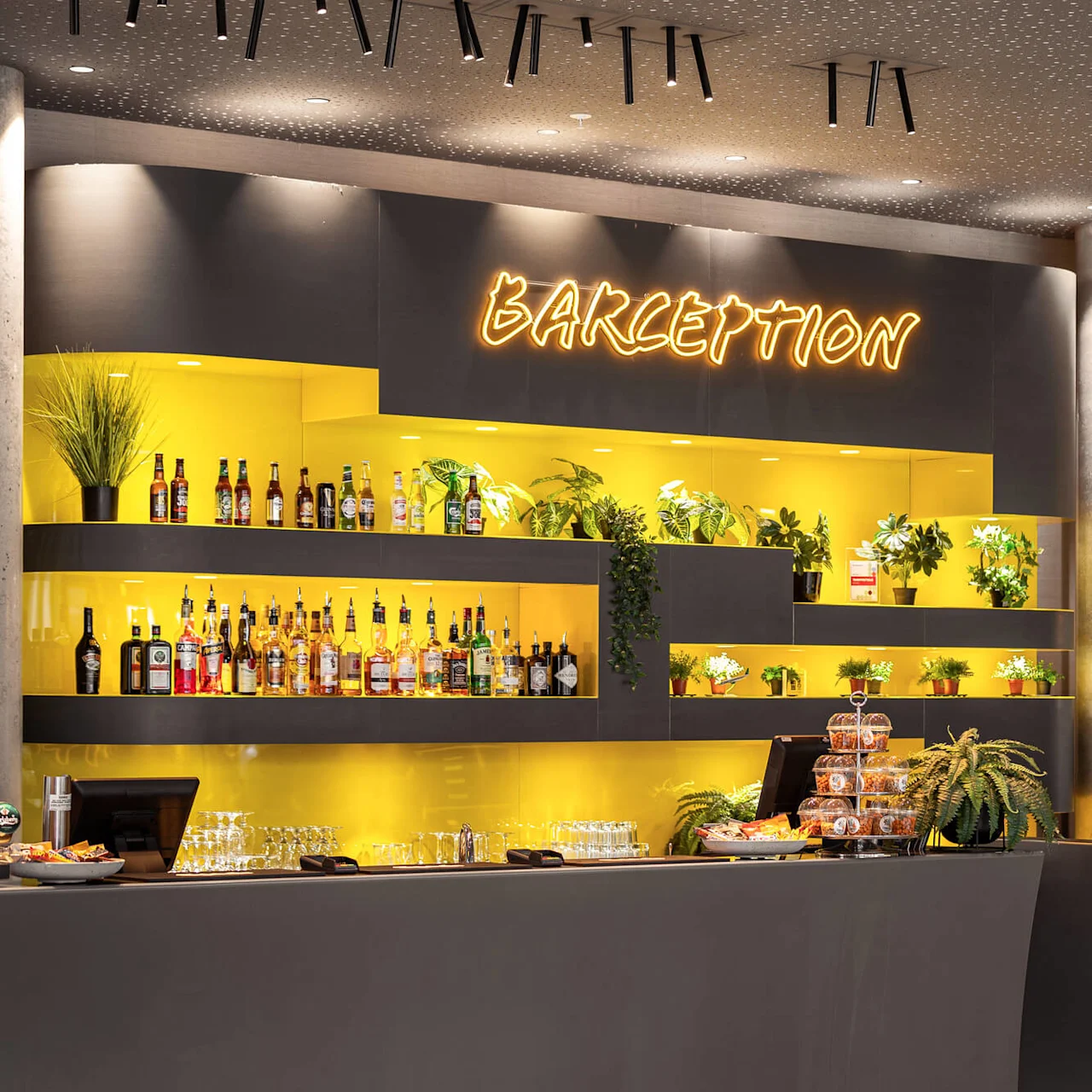Bar with yellow-lit shelves displaying bottles and plants. Neon sign reads "BARCEPTION". Wall-mounted screens show "Weather forecast Flesland", "Arrivals", and "Departures". Snacks and glasses on the counter.