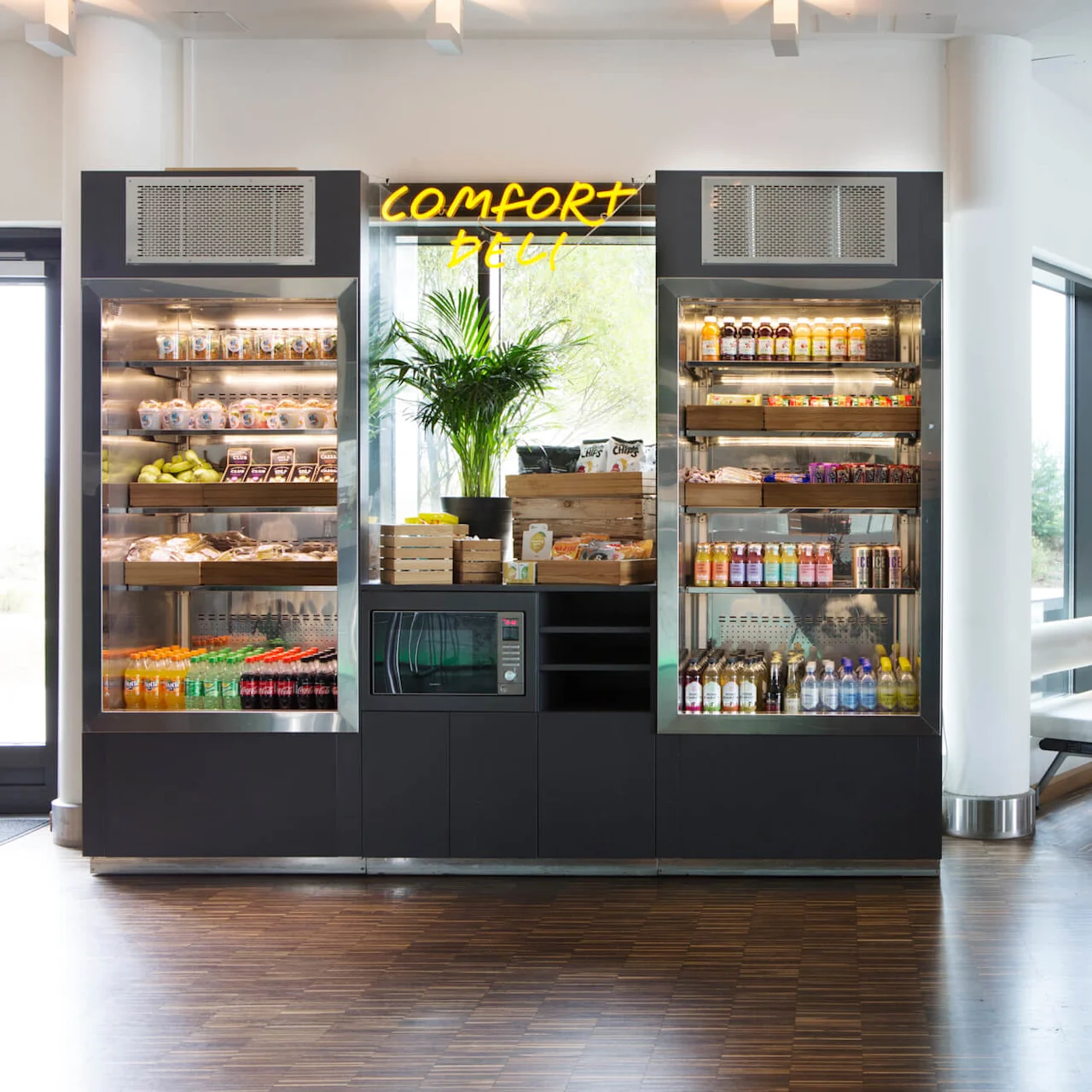 A vending area displays snacks, drinks, and a microwave under a "Comfort Deli" sign, set in a bright, modern lounge with chairs and large windows.