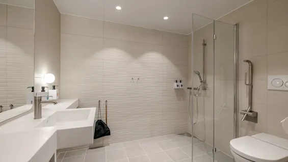 Modern bathroom featuring a white sink with a silver faucet, a glass-enclosed shower, and a wall-mounted toilet. Neutral tiles decorate the floor and walls, creating a sleek atmosphere.