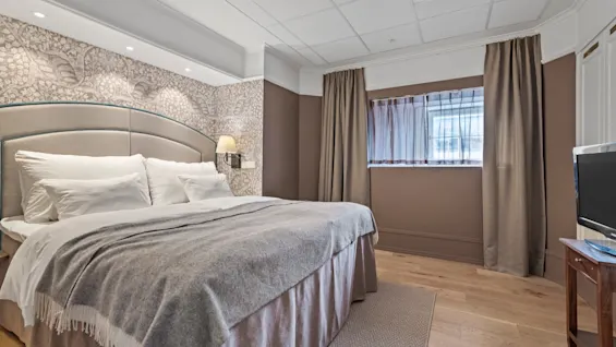 A comfortable hotel room with a large bed, patterned wallpaper, and a window, inviting guests to relax and unwind.