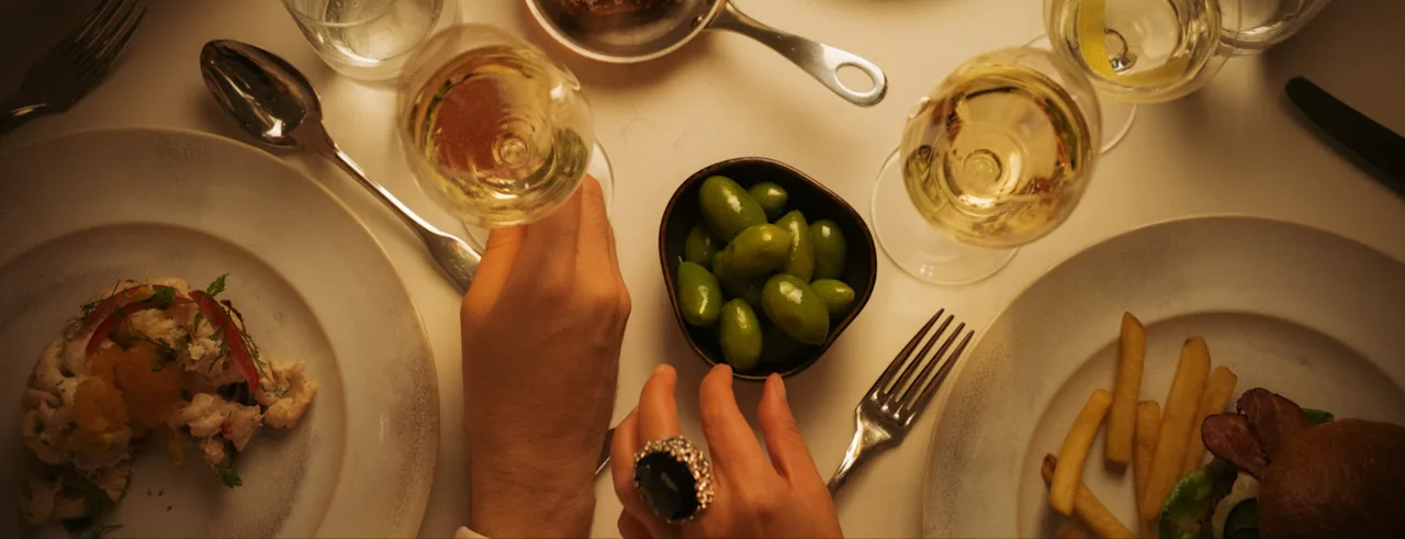 En varm, innbydende middagsscene på Hotel Kämp i Helsingfors, med hender som strekker seg etter vinglass blant ulike deilige retter.