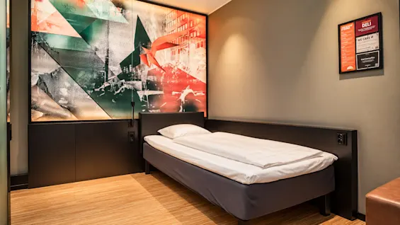Modern single hotel room featuring colorful wall art and wooden flooring.