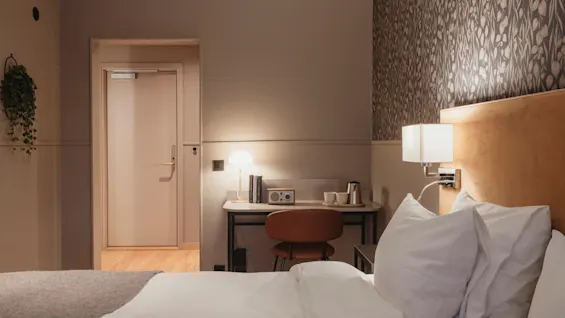 Ett mysigt hotellrum med en bekväm säng, en väl upplyst skrivbordsplats och en dörr som leder till en annan del av rummet.