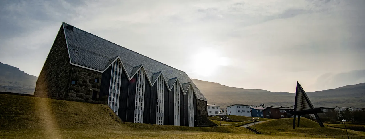 En moderne kirke med spidse taglinjer i et åbent græslandskab under en overskyet himmel.