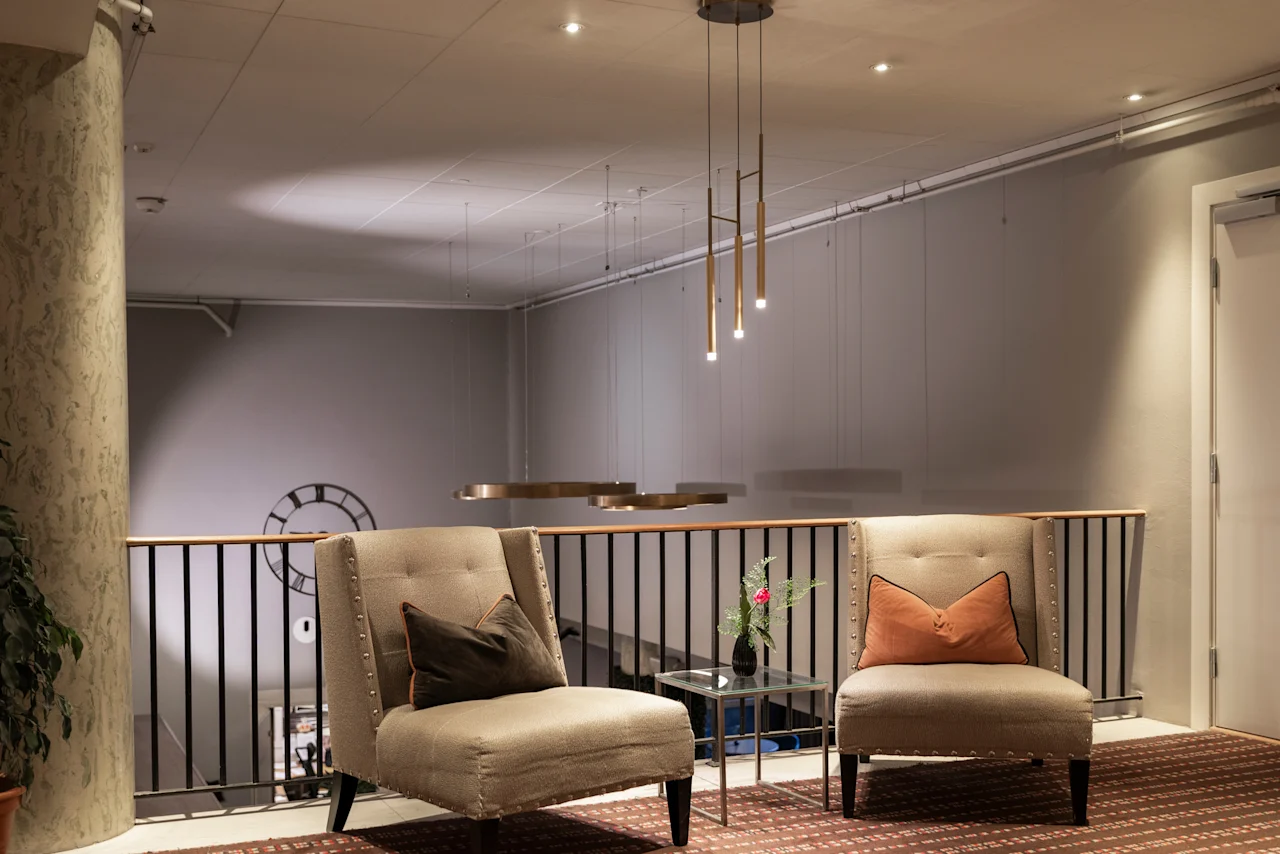 Home Hotel Grand Bodø lounge area with two comfortable armchairs, a small table, and modern lighting, overlooking a lower floor.