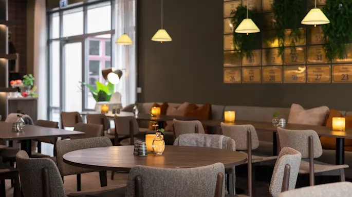 Et varmt og innbydende restaurantinteriør med komfortable sitteplasser, myk belysning og en dekorativ vegg med tall som 11, 26, 17, 28.