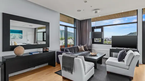 Quality Hotel Ulstein: Ett modernt vardagsrum med mysiga sittplatser, en TV och stora fönster som visar ett vackert bergslandskap.