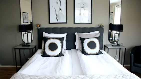 Modern hotel room featuring a neatly made double bed, stylish pillows, mirrors, and wall art.
