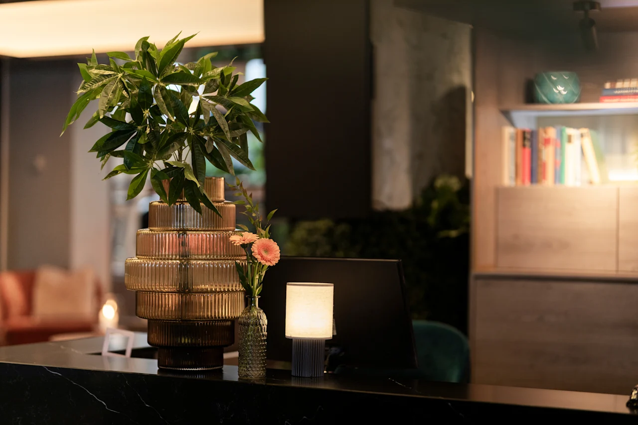 A stylish and inviting reception desk at Home Hotel Grand Bodø, featuring lush greenery, delicate flowers, and soft lighting.