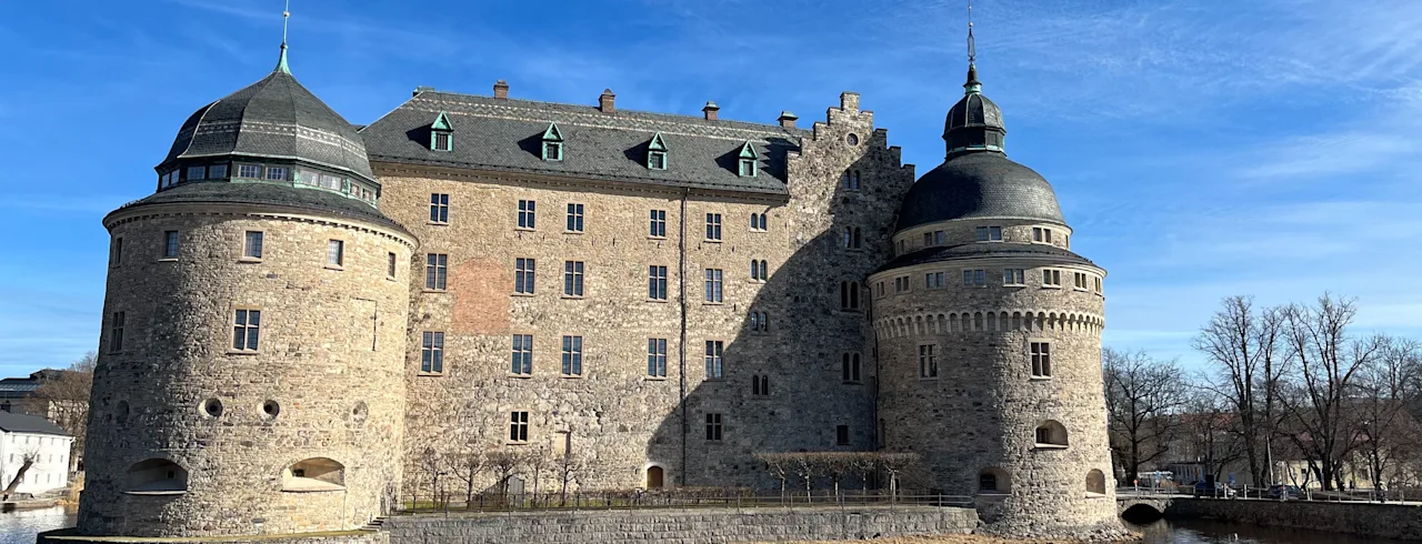 A majestic stone castle with prominent round towers, surrounded by water, under a clear blue sky. Things to do in Örebro.