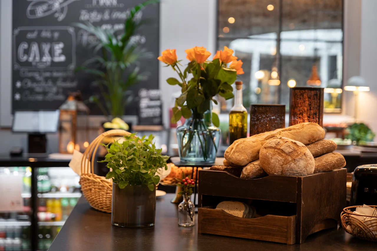 Home Hotel Grand Bodø: A delightful breakfast spread with fresh bread, a vase of orange roses, and a chalkboard menu displaying 'CAKE'.